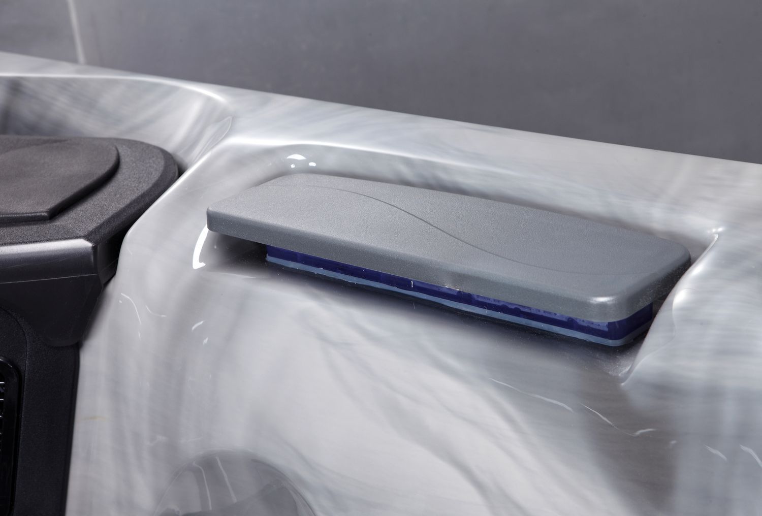 Close-up of a hot tub with a gray control panel cover. The tub is marbled gray and white.