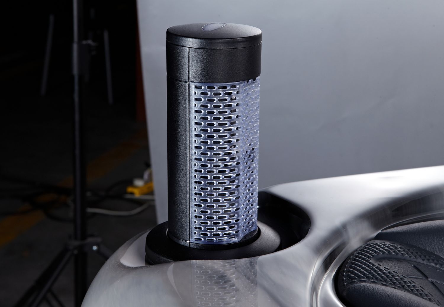 Black and silver cylindrical air purifier in a cup holder, studio setting.