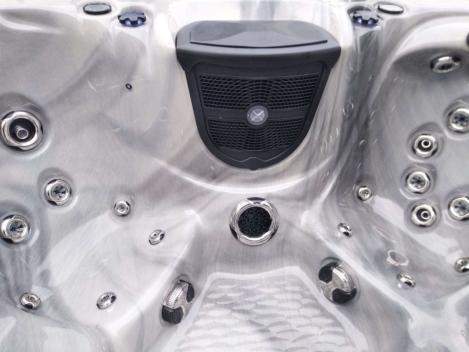 Close-up of a hot tub interior with gray marbled shell, jets, and a central speaker.