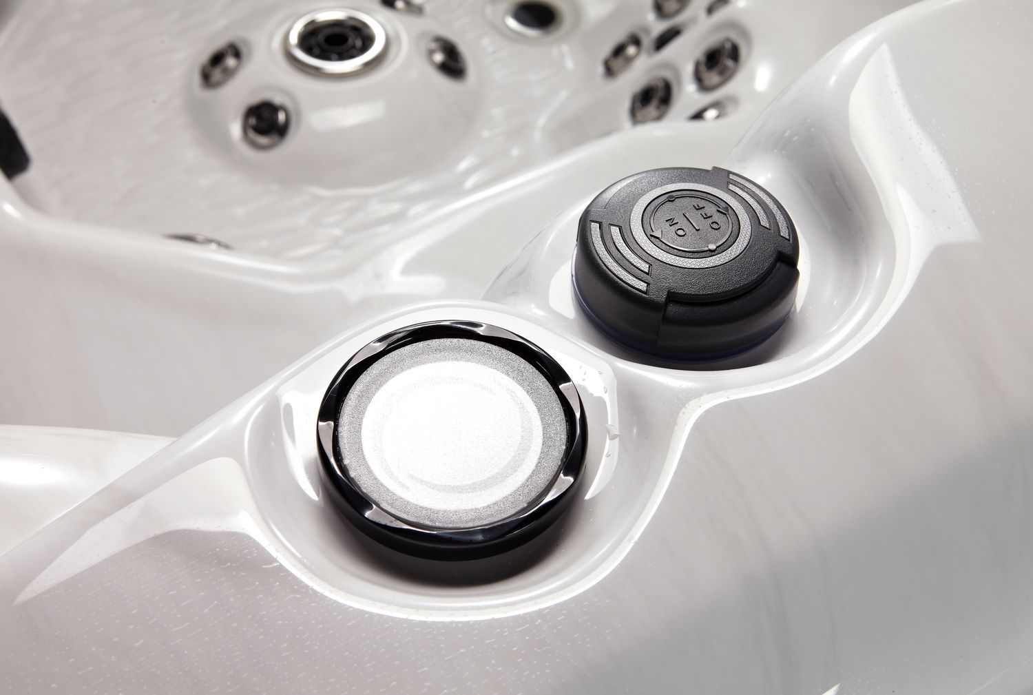 Close-up of a white hot tub interior featuring two black control dials. Water jets and curved armrests are visible.
