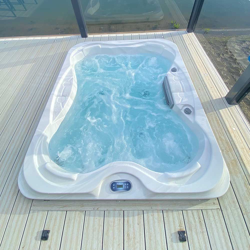 White hot tub filled with bubbling blue water on a wood deck.