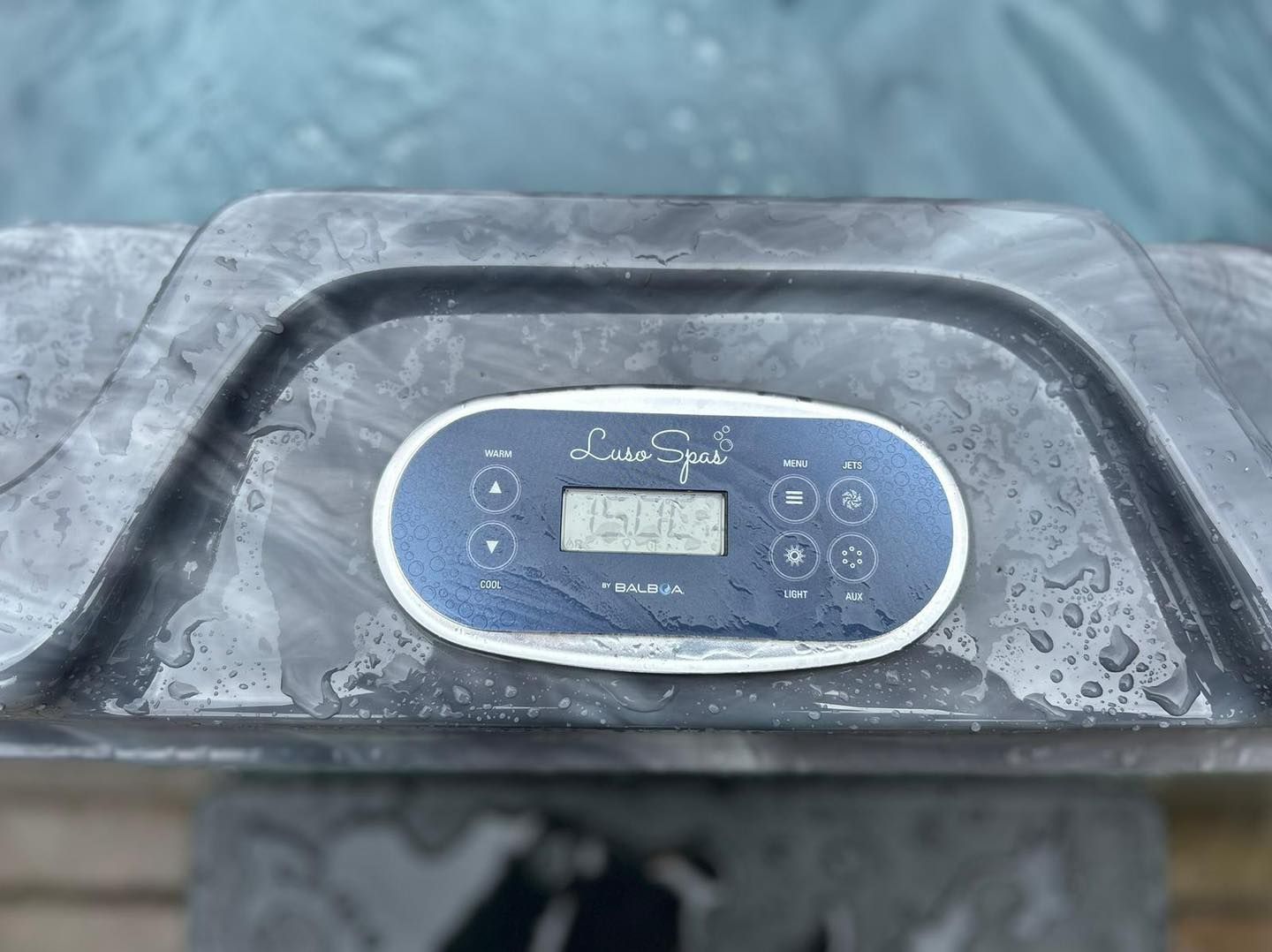 Hot tub control panel with digital display and buttons. Gray, wet surface.
