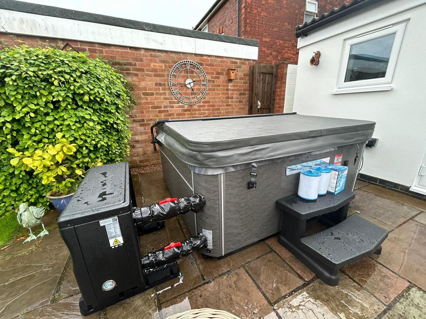 A hot tub with cover, steps, and water treatment system on a patio, outdoors.