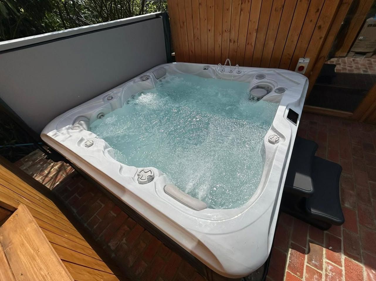 Hot tub on a brick patio with bubbles. Cover is partially open, and steps are on the side.