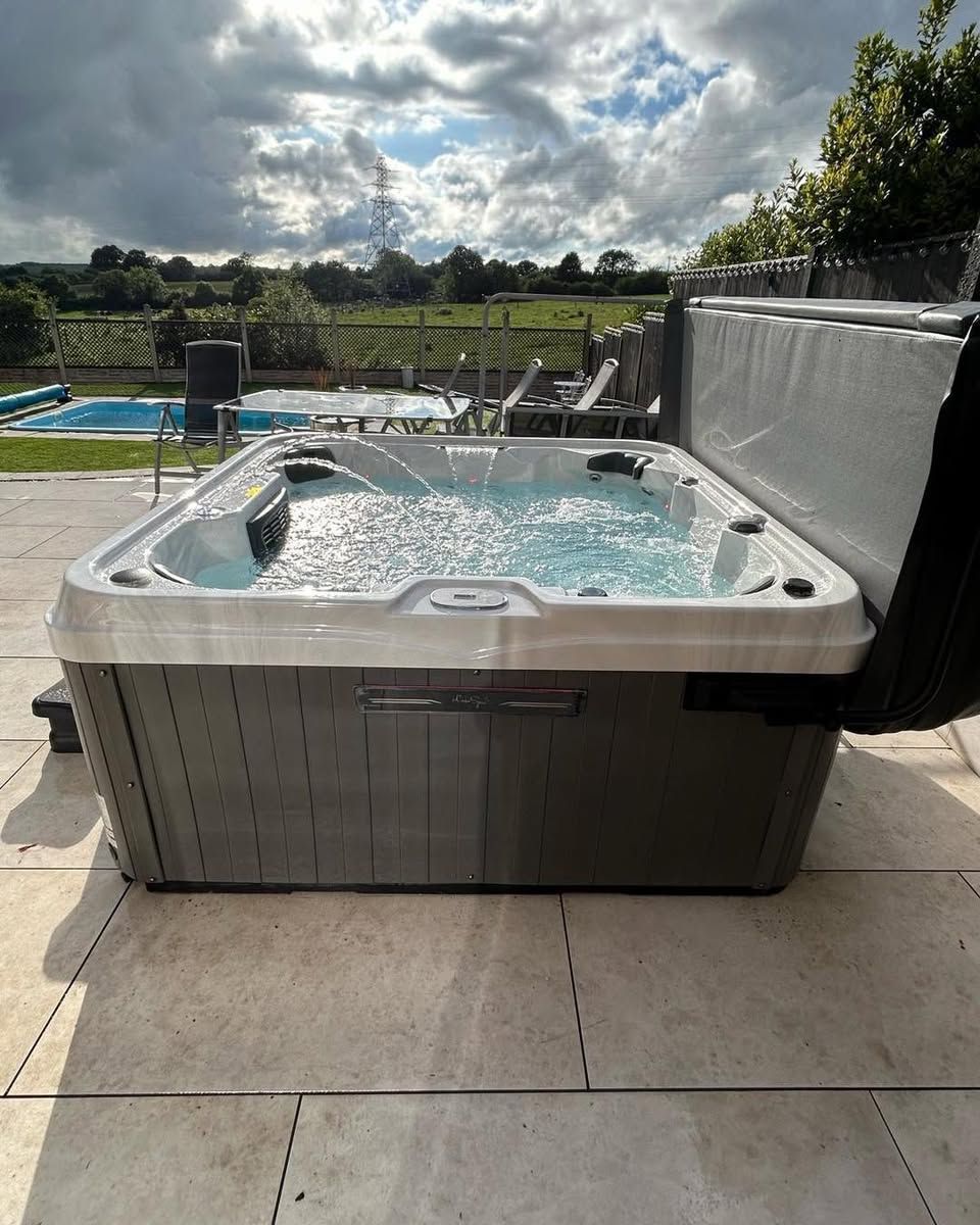Hot tub on patio with partially open cover, overlooking a pool and rural landscape.