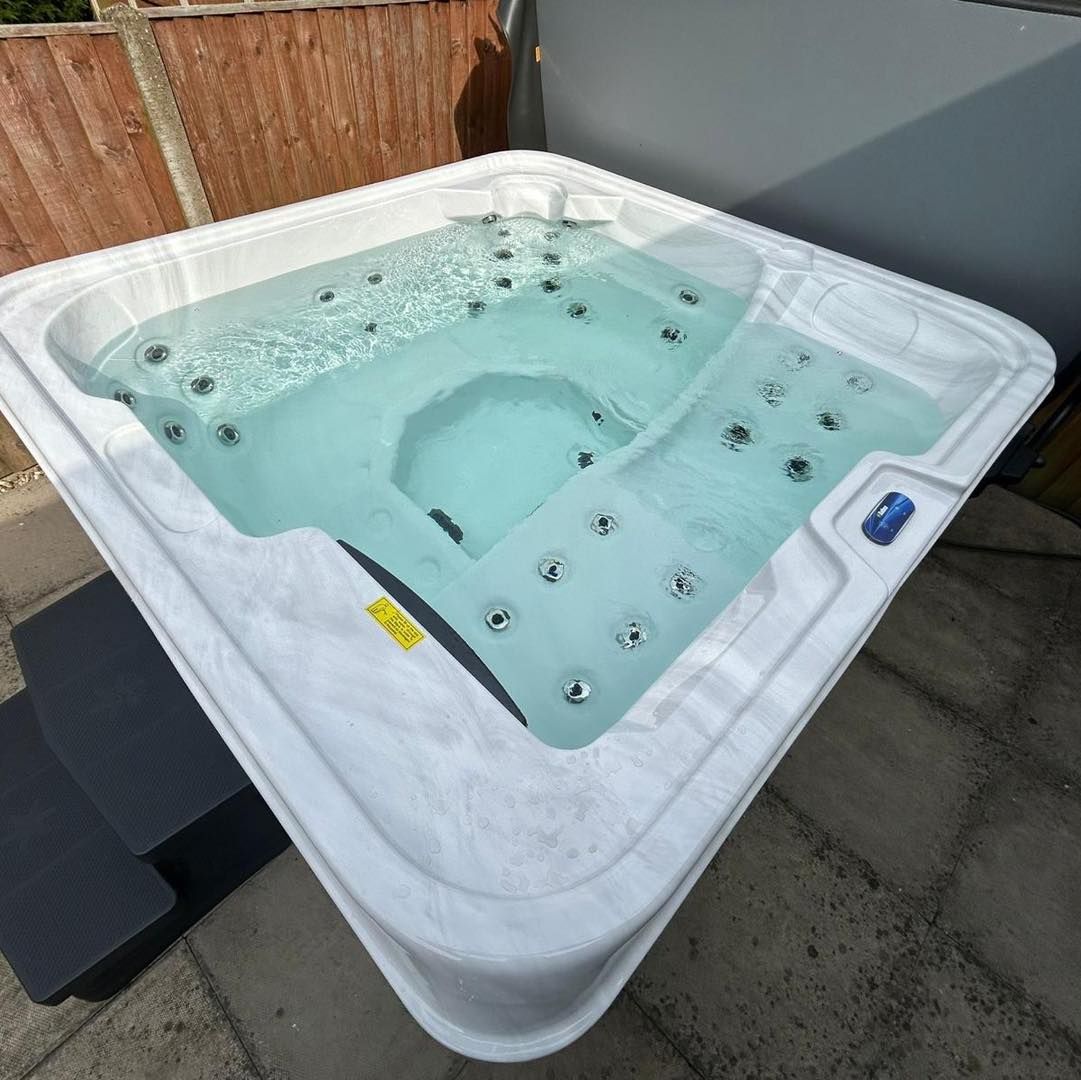 Square white hot tub filled with water on patio, steps on the left.
