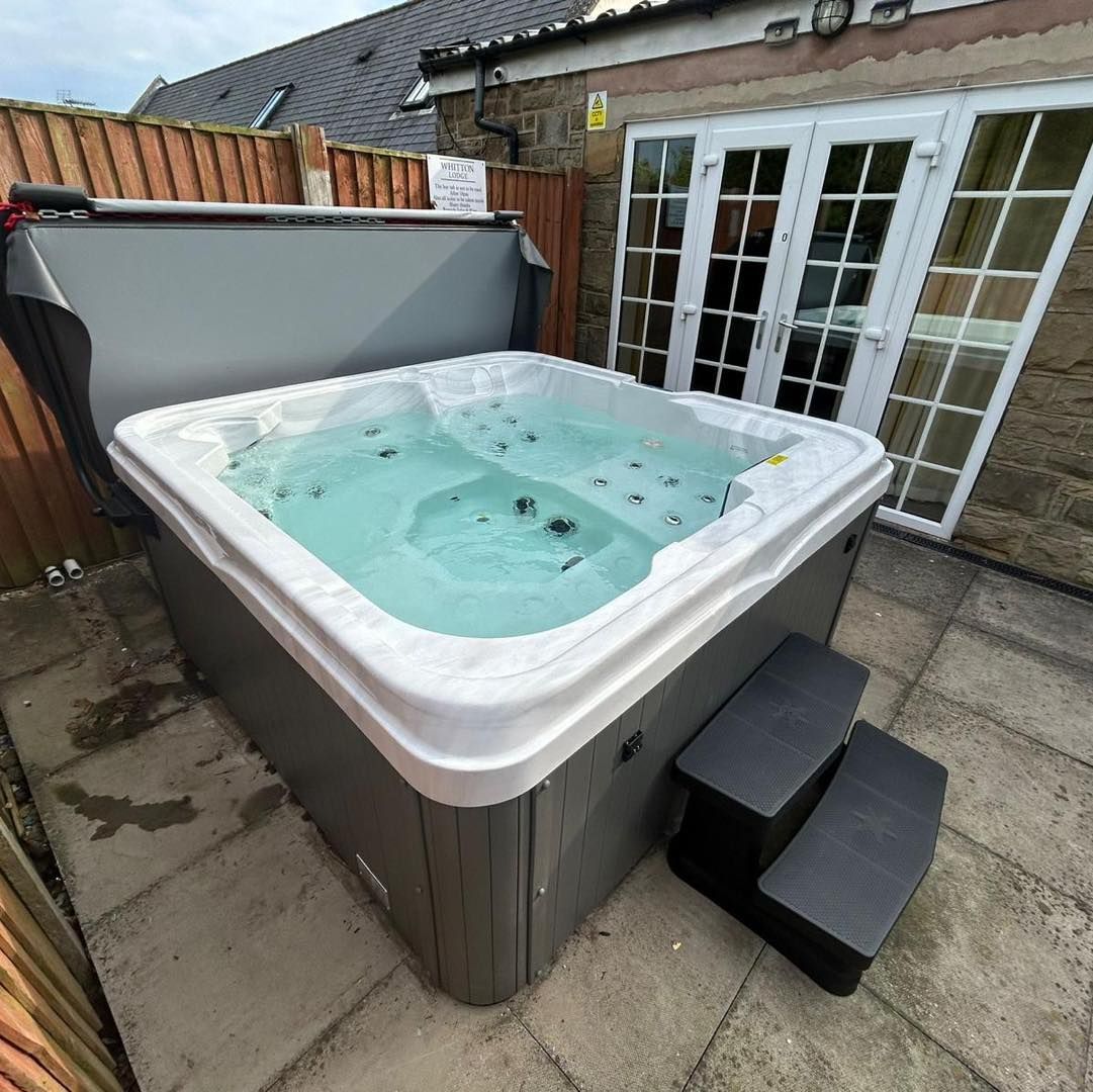 Hot tub on patio with steps, cover open. Grey siding and white trim surround the spa.