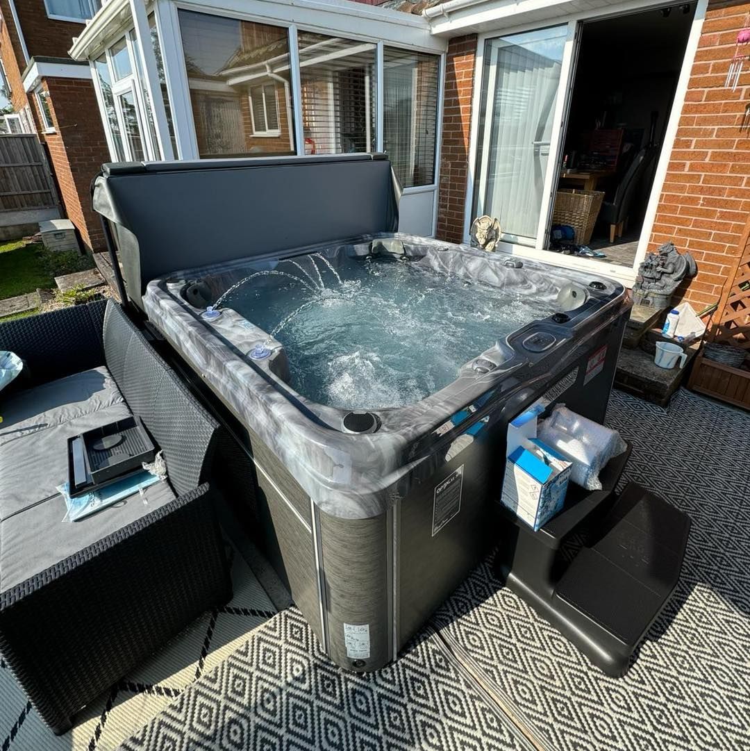 Hot tub with open cover, steps, and nearby seating in a backyard patio setting.