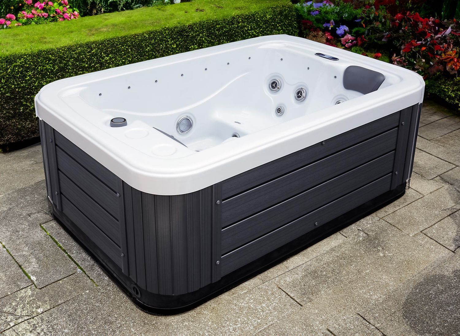 Hot tub on a stone patio with a dark grey exterior and white interior.