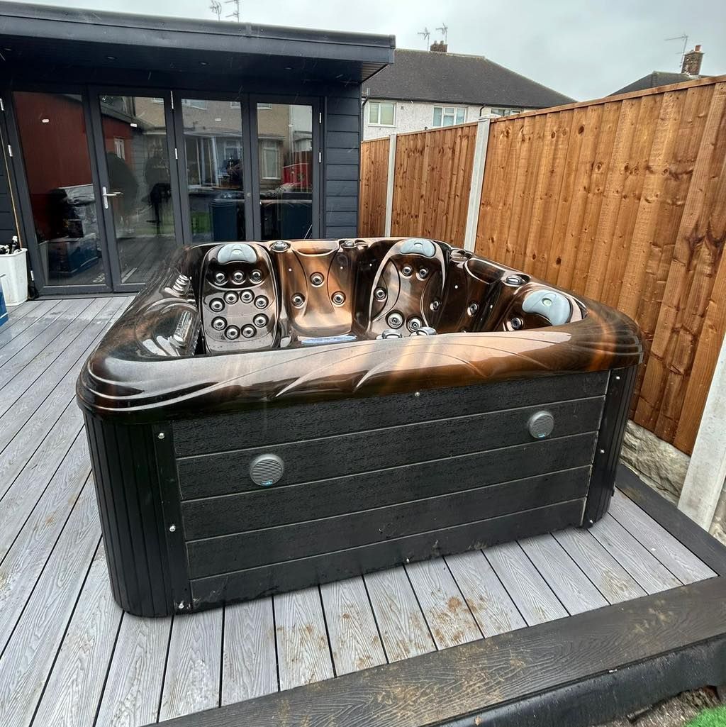Hot tub on a wooden deck next to a fence and a building with glass doors.