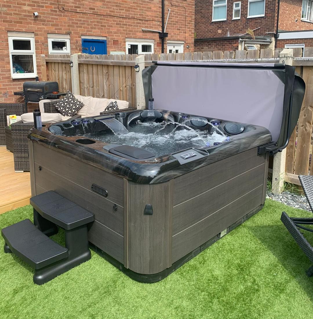 Hot tub with bubbling water, partially open lid, set in a backyard with green lawn.
