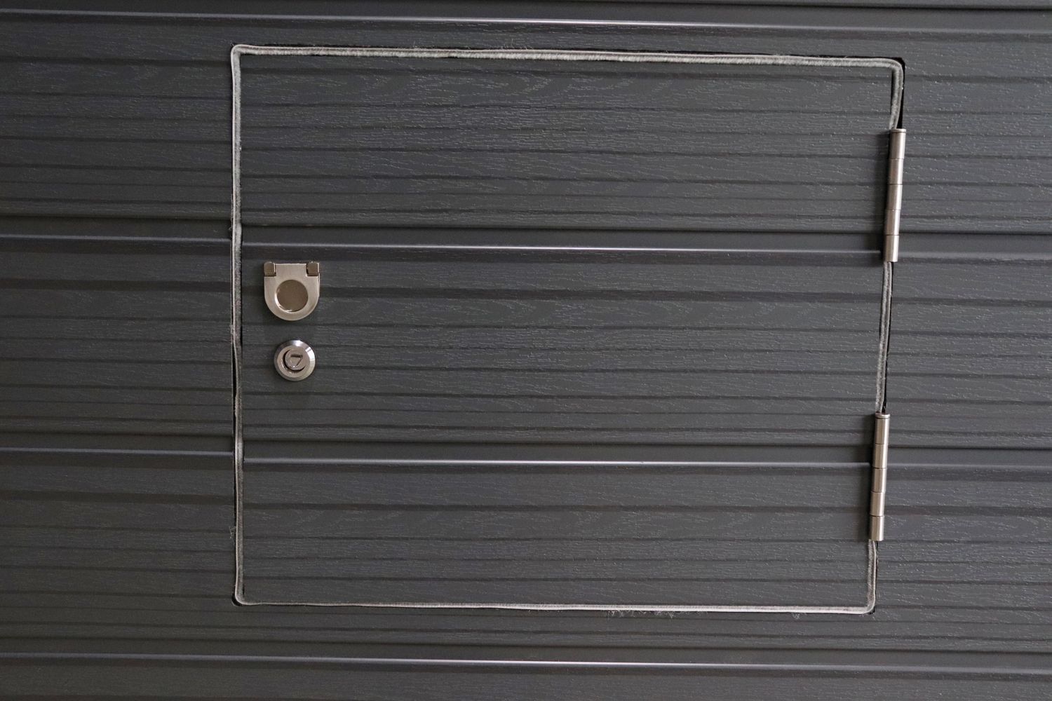 Gray metal panel with small access door, hinges, lock, and keyhole.