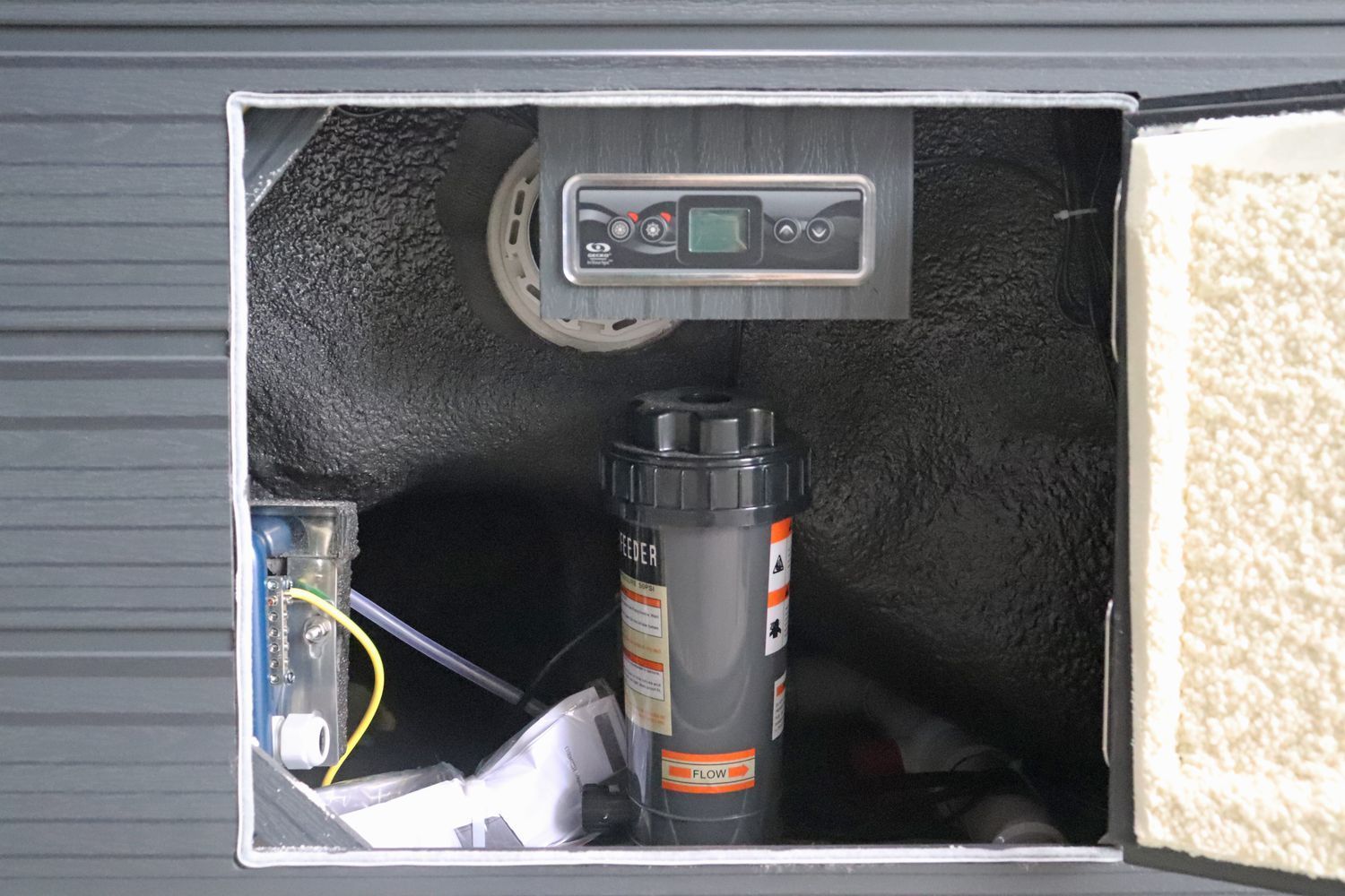 Inside an equipment compartment, control panel, filter, and plumbing. Dark interior, open door with insulation.