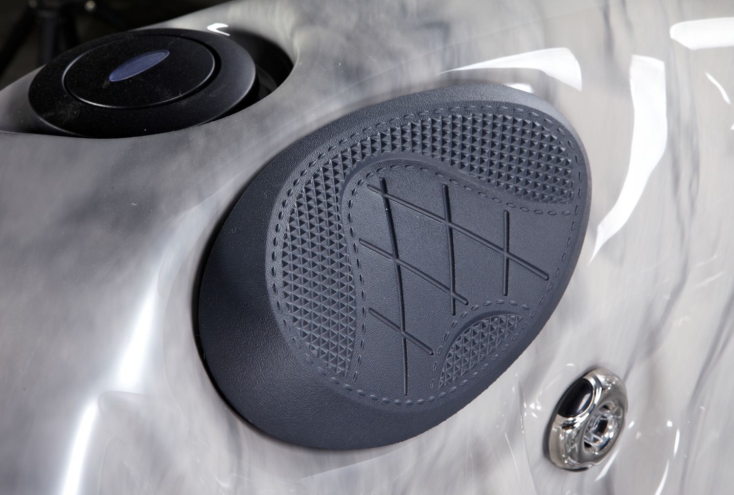 Close-up of a gray hot tub interior with a textured grip pad, control button, and jet.