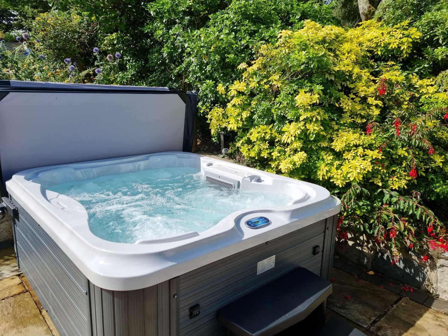 Hot tub outdoors with bubbling water, surrounded by green and yellow foliage.