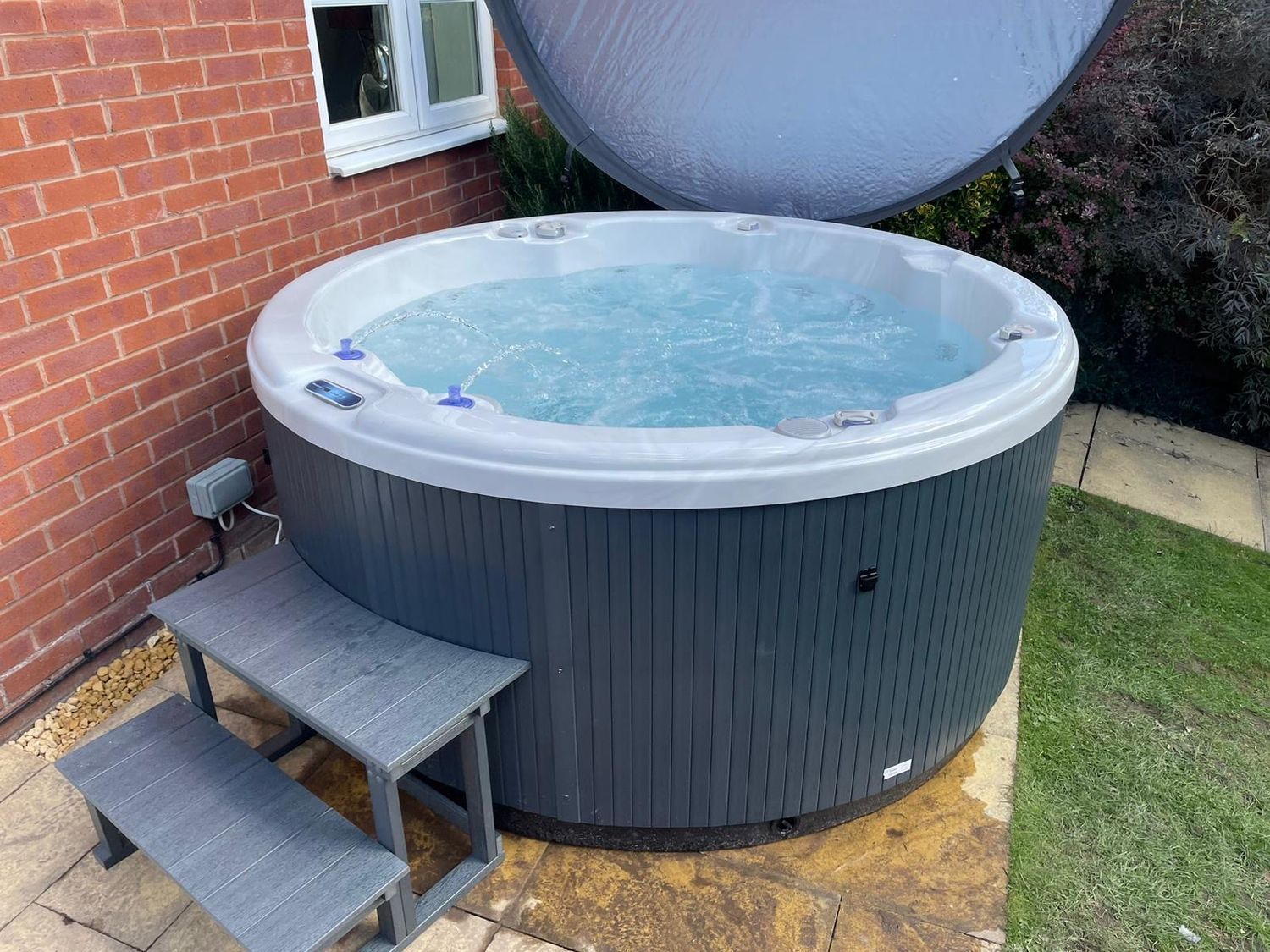 A round, gray hot tub with bubbling water, set beside a brick wall and steps.