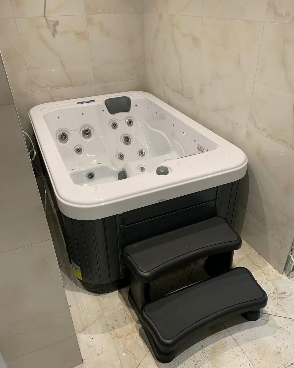 A dark gray hot tub with two steps in a tiled corner.