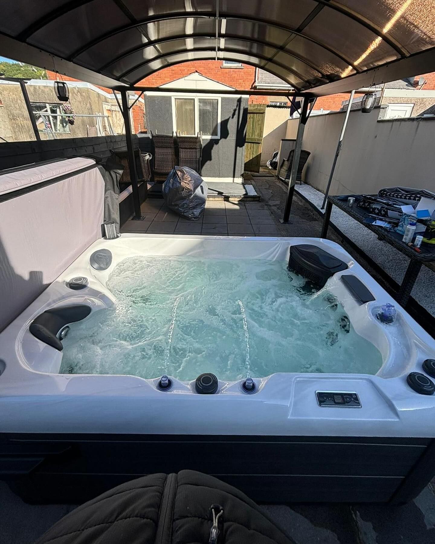 Hot tub bubbling on a patio, under a canopy. A black control panel is visible.