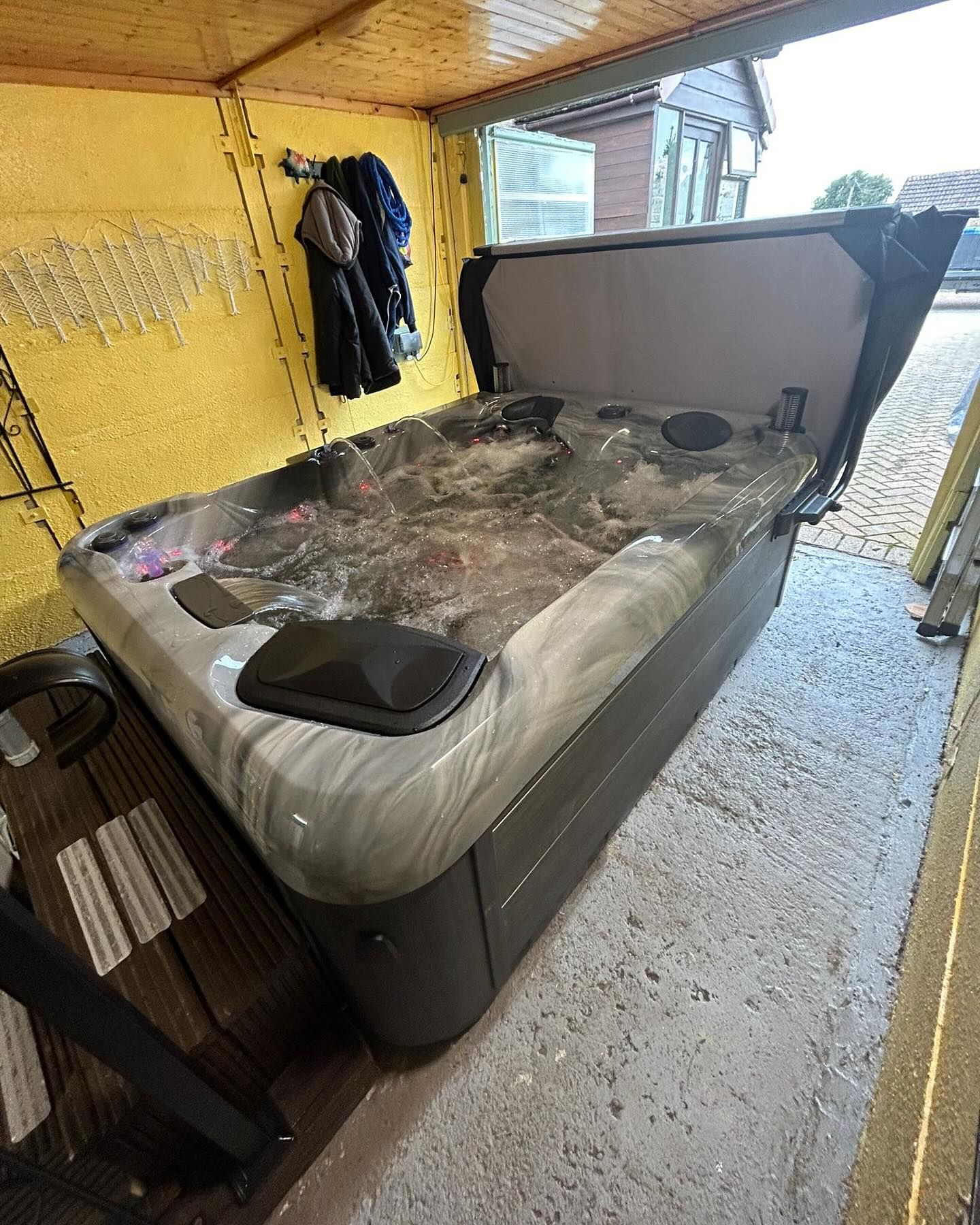 Hot tub with the lid open, placed under a wooden overhang.