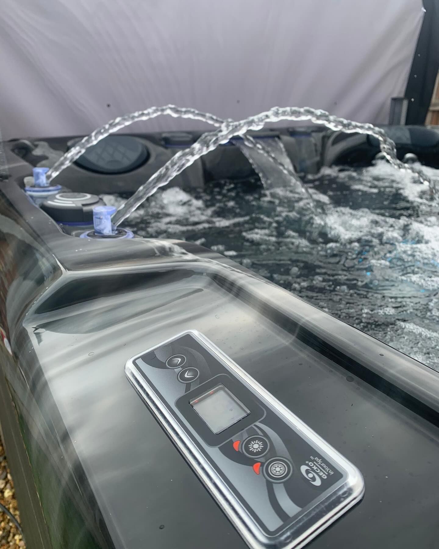 Hot tub with water jets, control panel visible, outdoors.