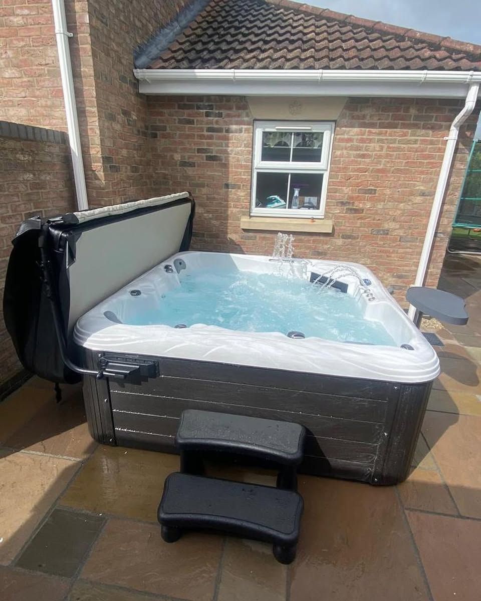 Hot tub on a patio with steps, next to a brick building. The cover is open, and water is bubbling.