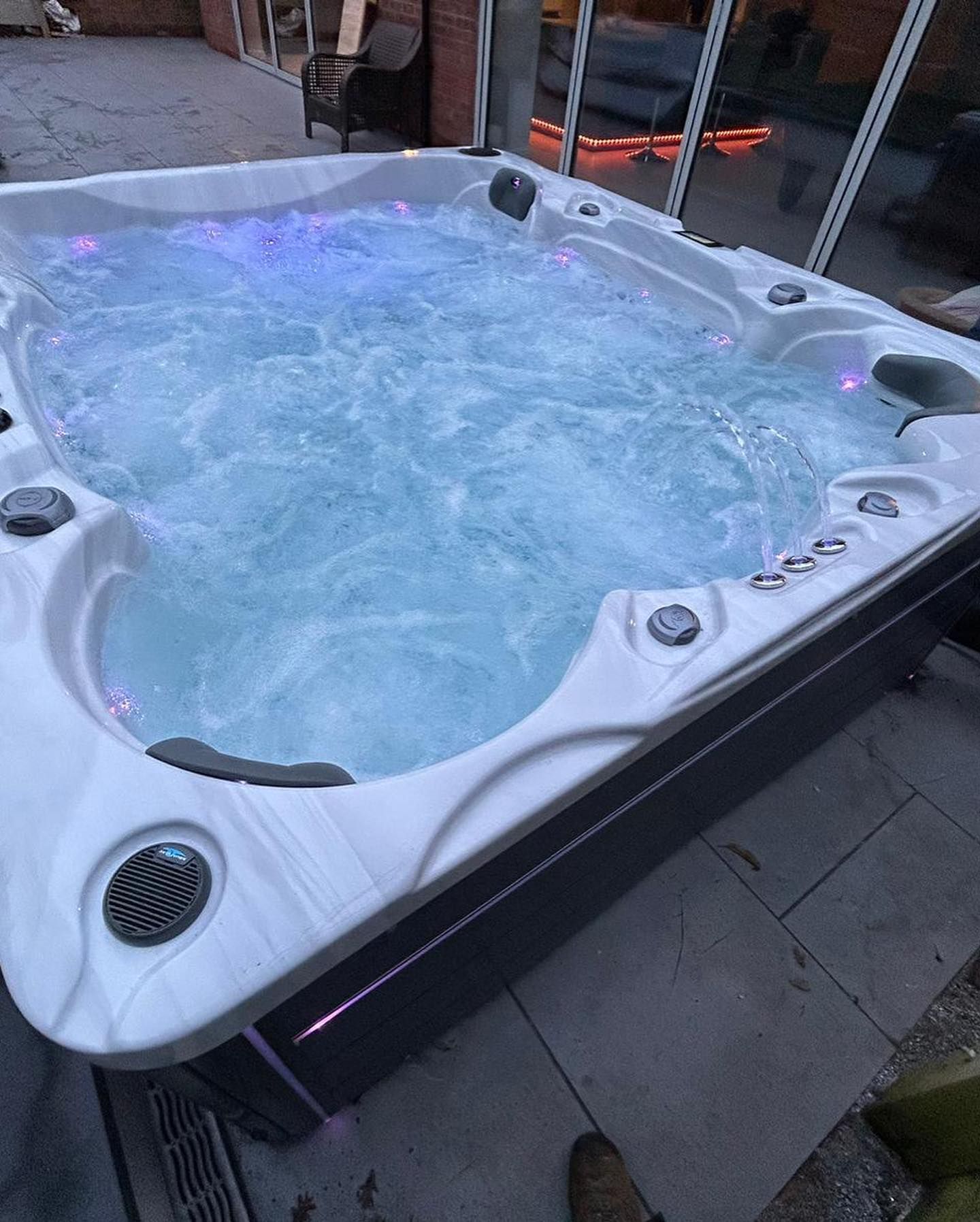 Bubbling hot tub with blue and purple lights, set on a patio.