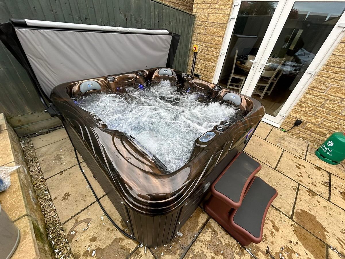 A hot tub bubbling in an outdoor patio setting, near a door. A two-step stool is in front.