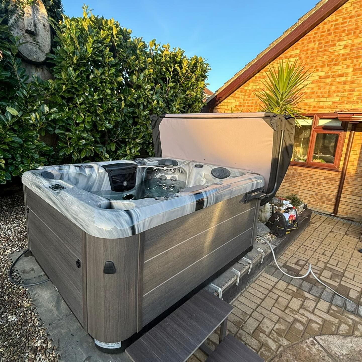 Hot tub with open cover, set on patio in a sunny backyard.