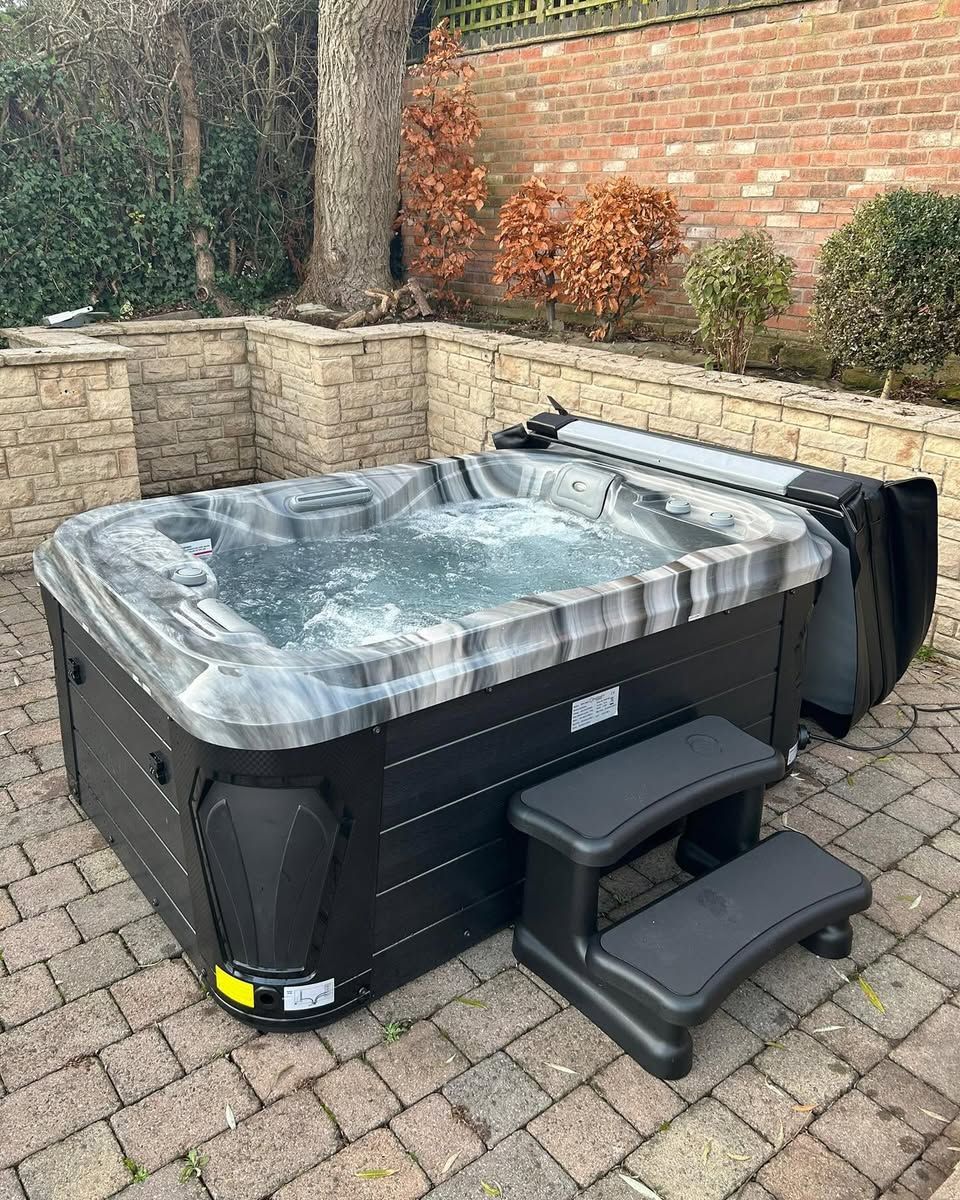 Black hot tub with gray accents, steps, and open cover in a brick patio setting.