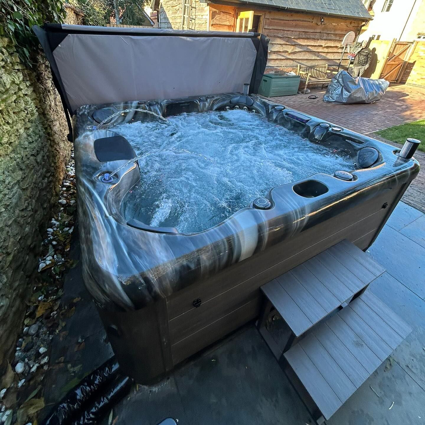 Hot tub with bubbling water; brown and gray exterior, steps on the side, set outdoors.