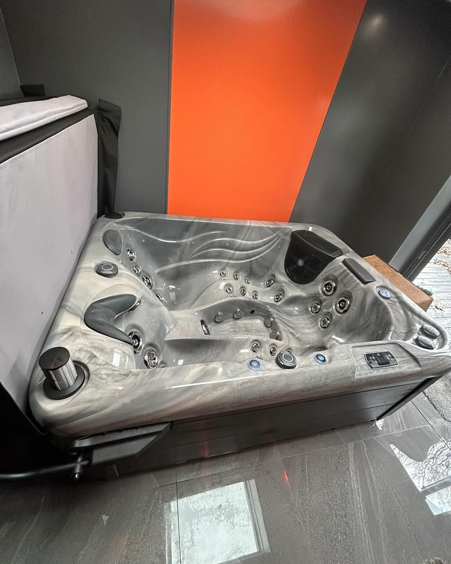 A grey and black hot tub with multiple jets, placed near a wall with an orange accent.
