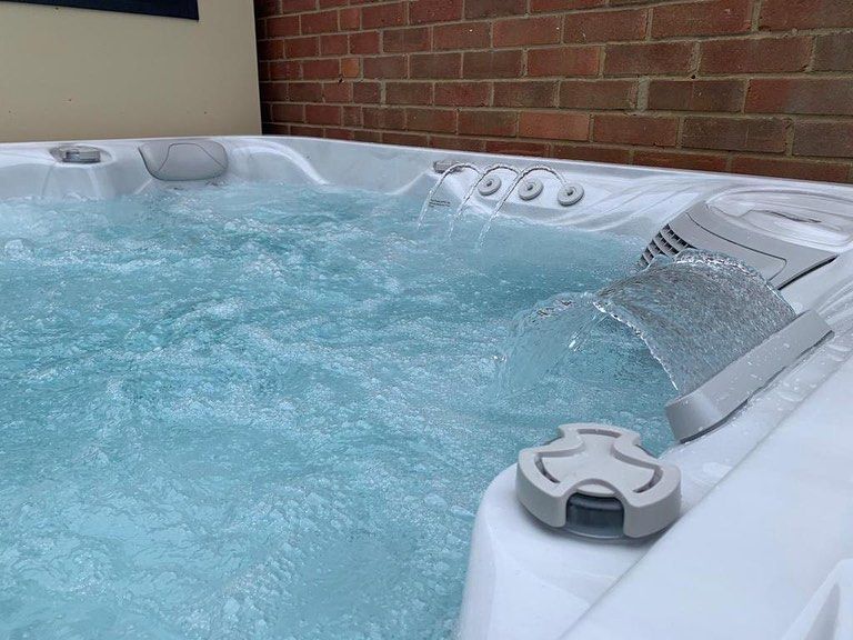 Bubbling hot tub with white interior, brick wall background. Water sprays from jets.