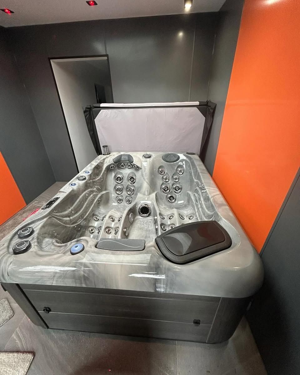 A hot tub with opened cover in a room with gray, orange walls.