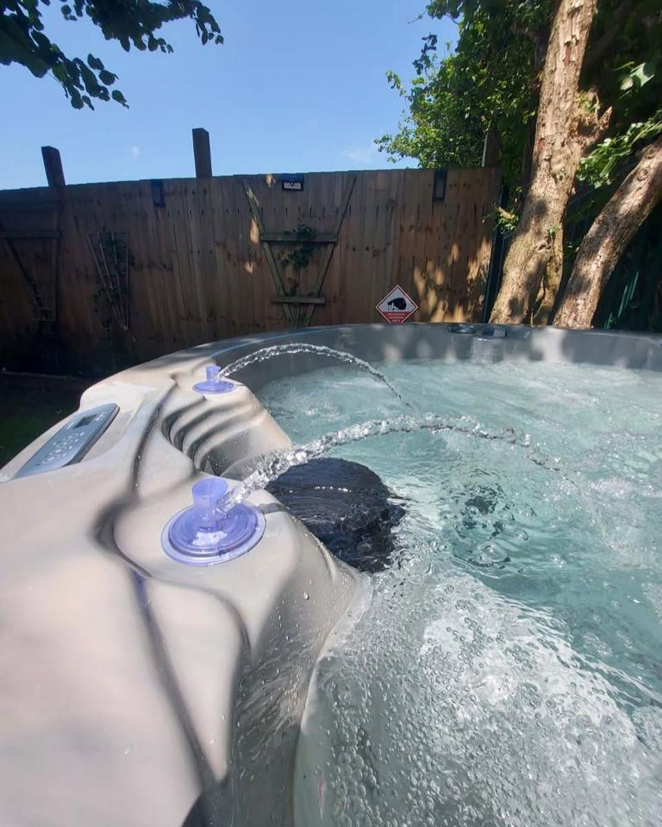 Hot tub with water jets active, set outdoors, with wooden fence and tree in background.