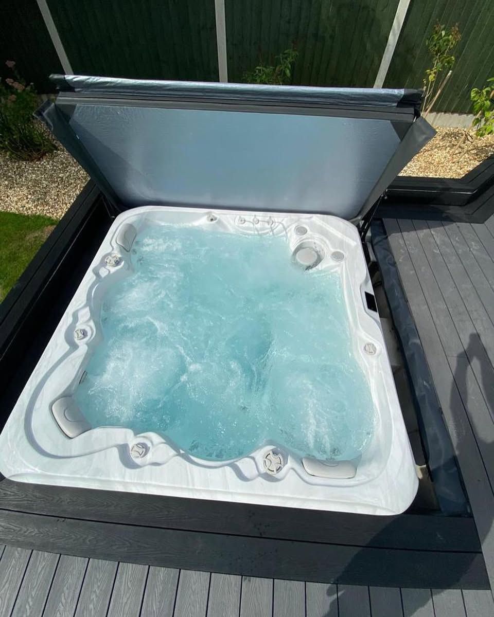 Hot tub filled with water, lid open, set into a grey wooden deck.