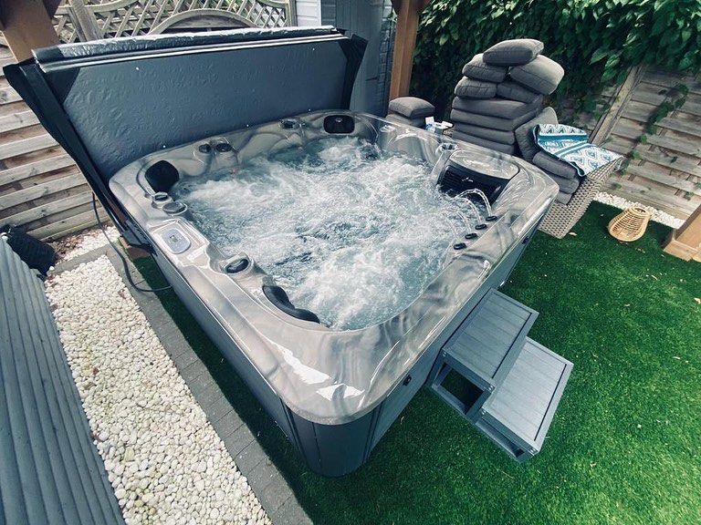 A bubbling hot tub on green artificial turf next to a gravel path with steps leading into it.