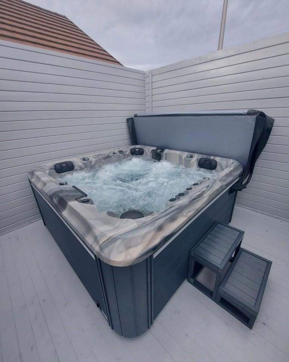 Hot tub with bubbling water, dark gray exterior, next to steps, on a white wooden deck.