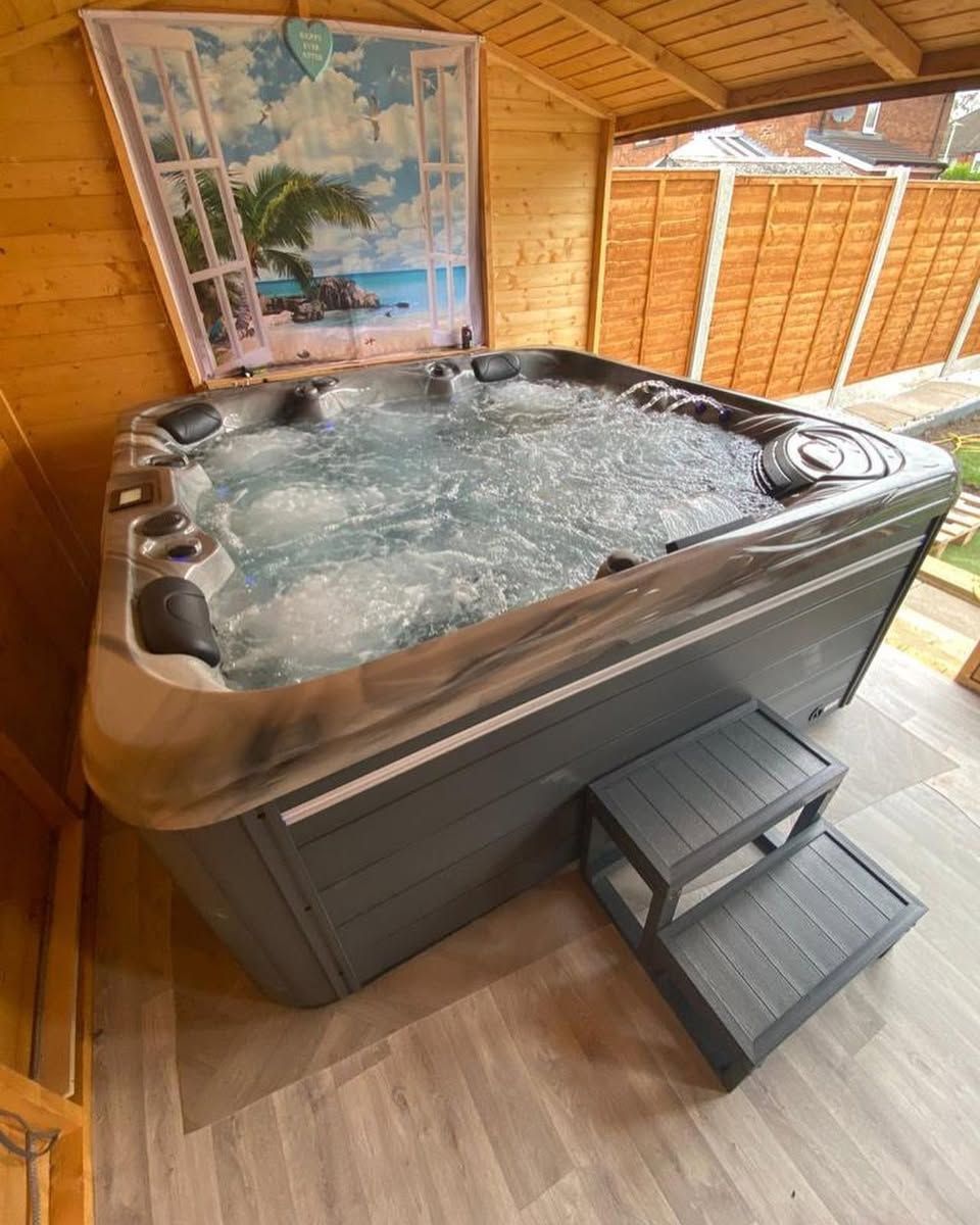 Hot tub with bubbling water inside a wooden shed, next to steps. A tropical landscape decorates the shed's wall.