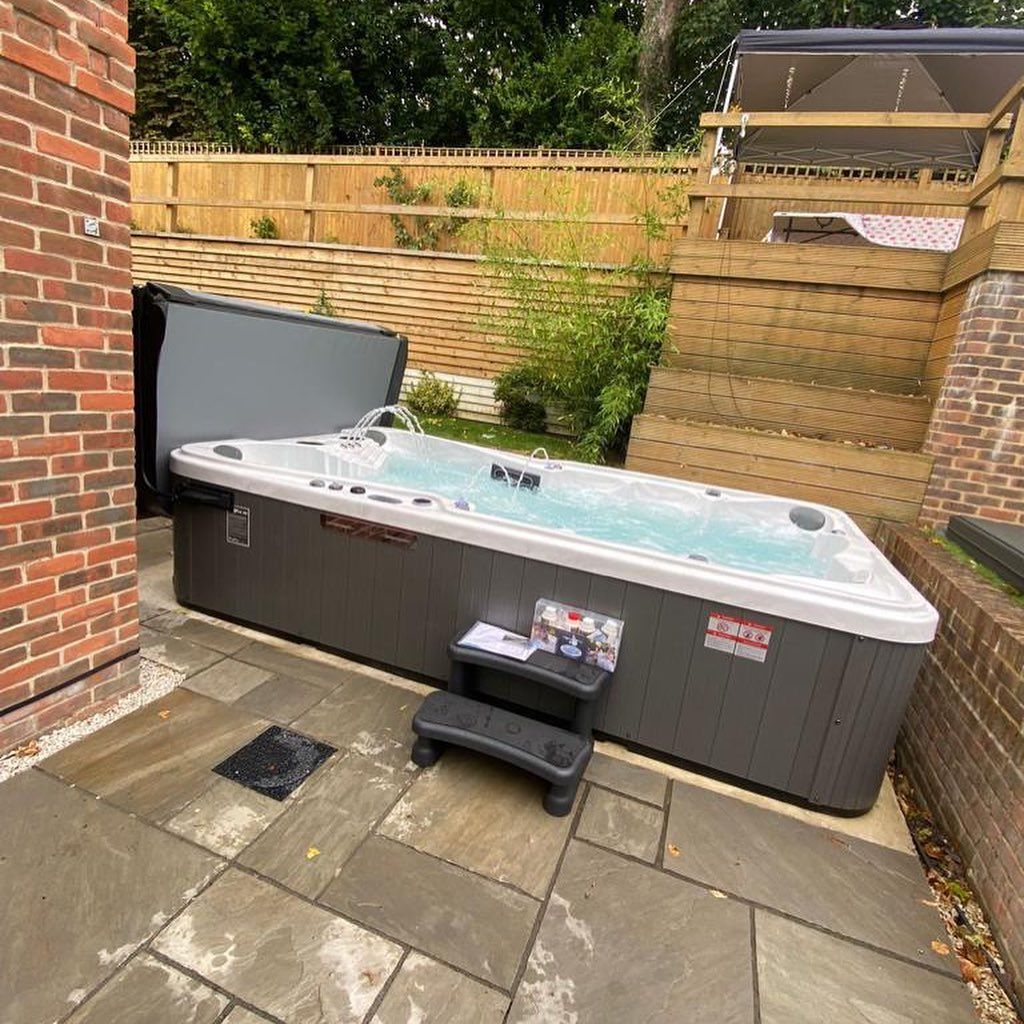 Hot tub on a patio with steps. Partially open cover, brick wall, and wooden fence in background.