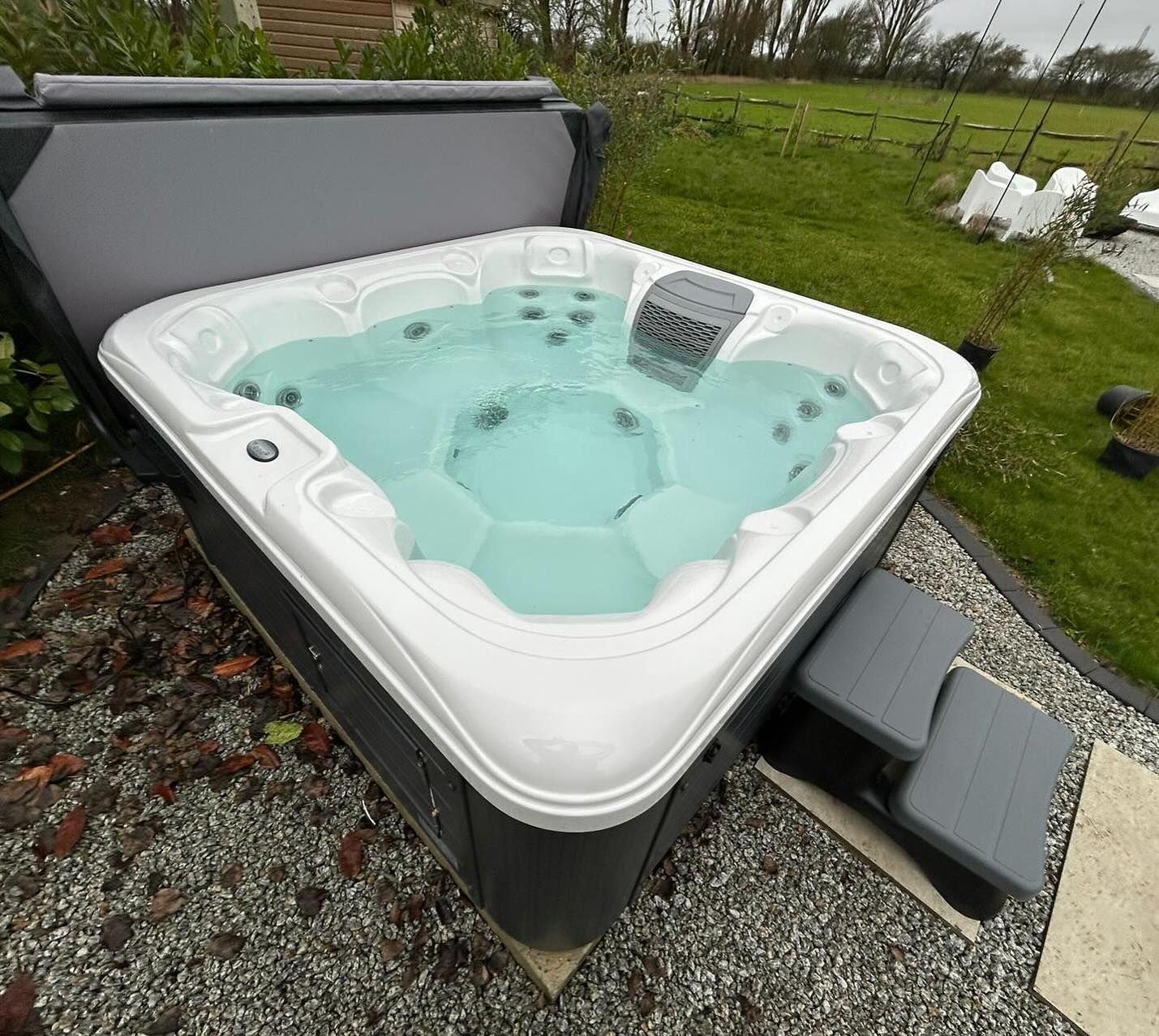 Hot tub with open cover, filled with turquoise water, outdoors. Gray steps are in front.