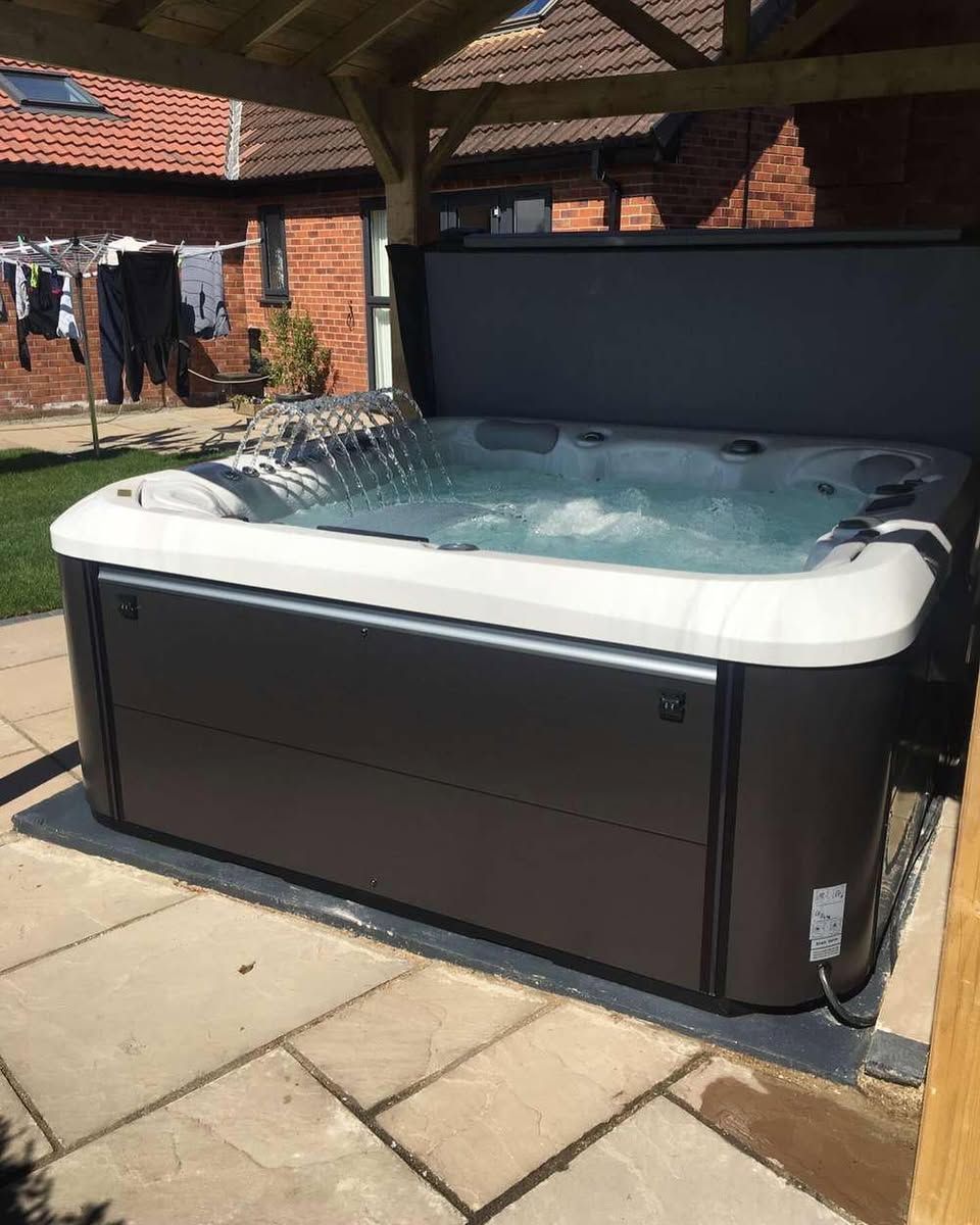 Hot tub with the cover open, placed on stone patio, under a wooden structure.
