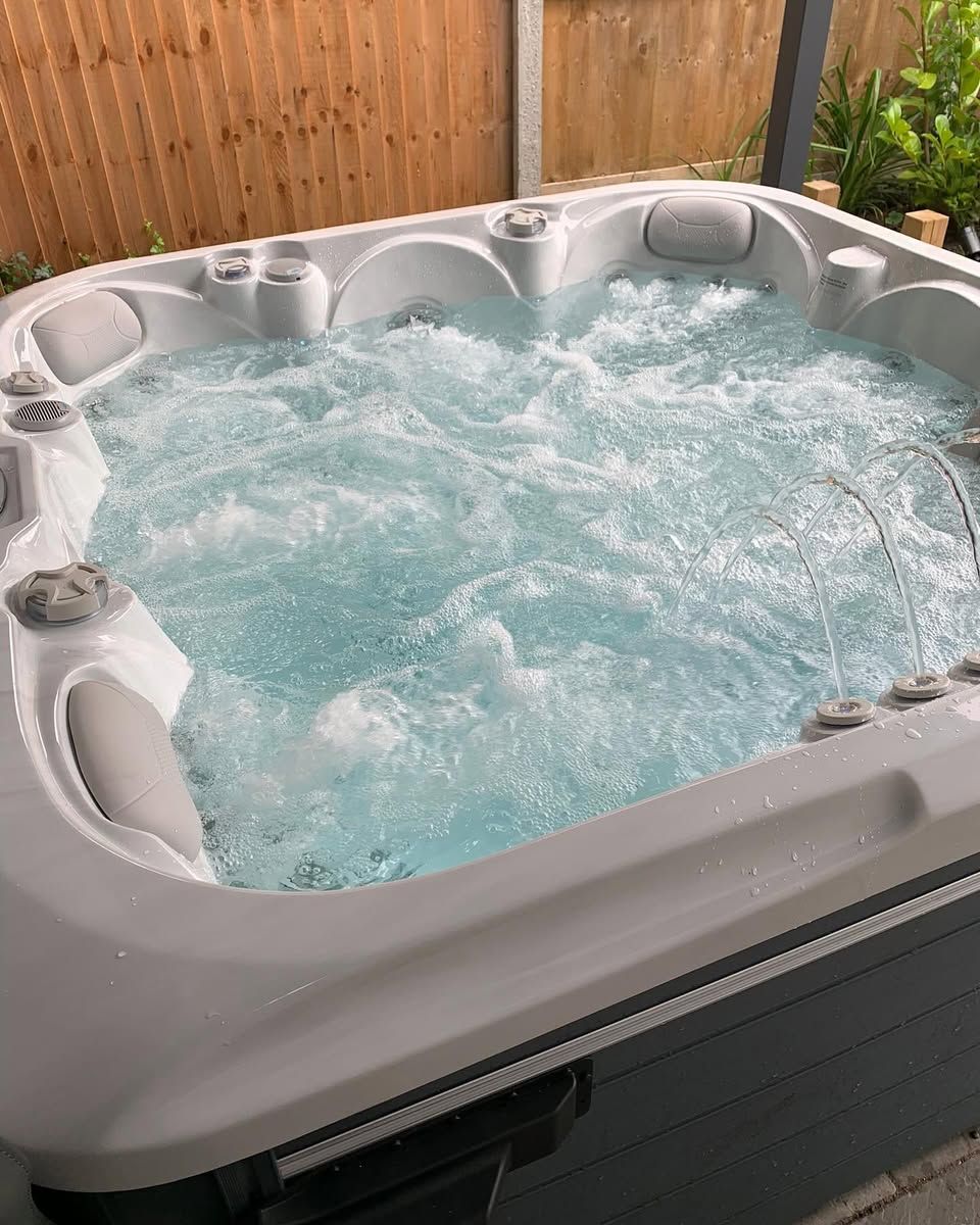 Hot tub with bubbling blue water outdoors. Grey and white tub surround.
