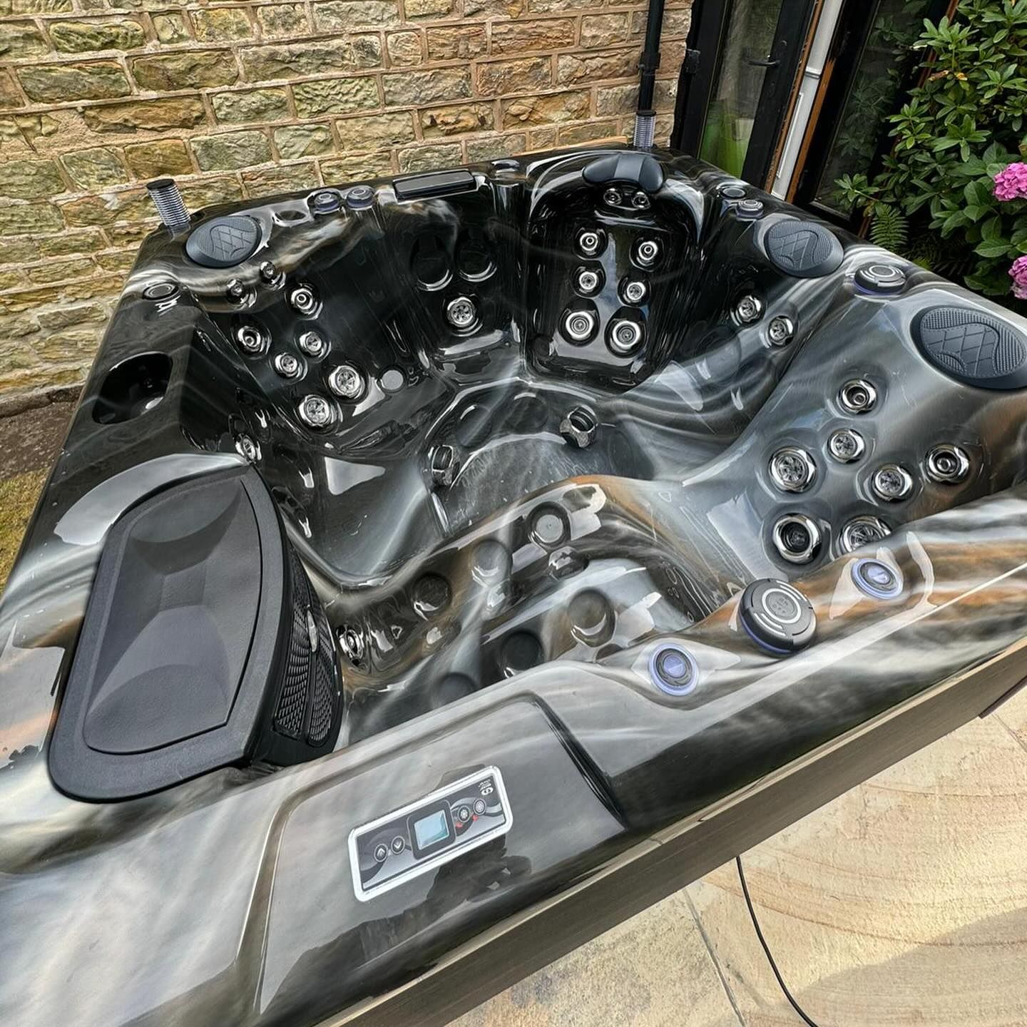 Hot tub, black and white marbled interior, with jets, control panel, and cup holder, outdoors near a brick wall.