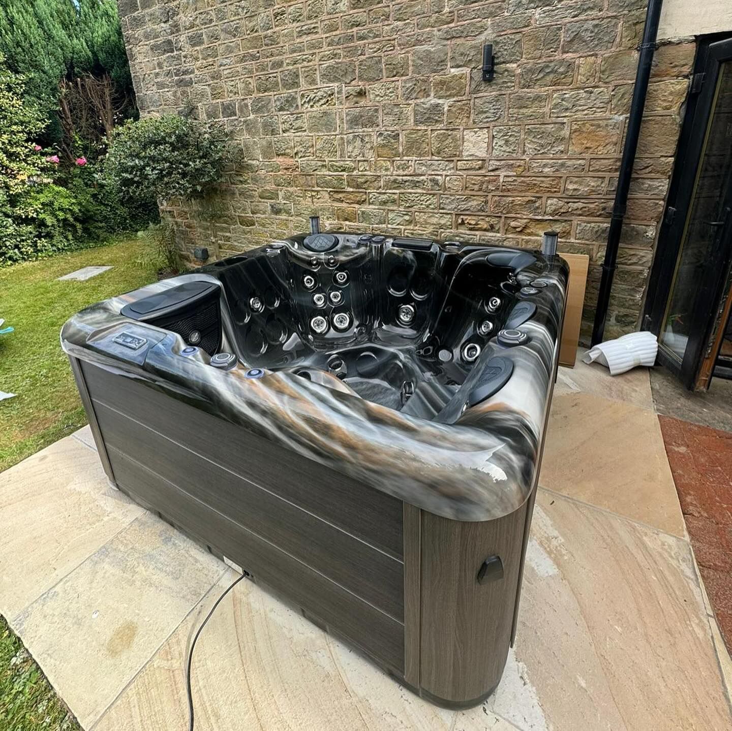 Hot tub with dark interior and patterned trim on stone patio near a stone wall.