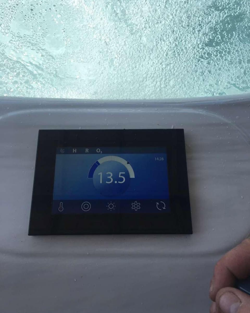 Hot tub control panel displays a water temperature of 13.5 degrees. Bubbles in the background, a hand in the foreground.