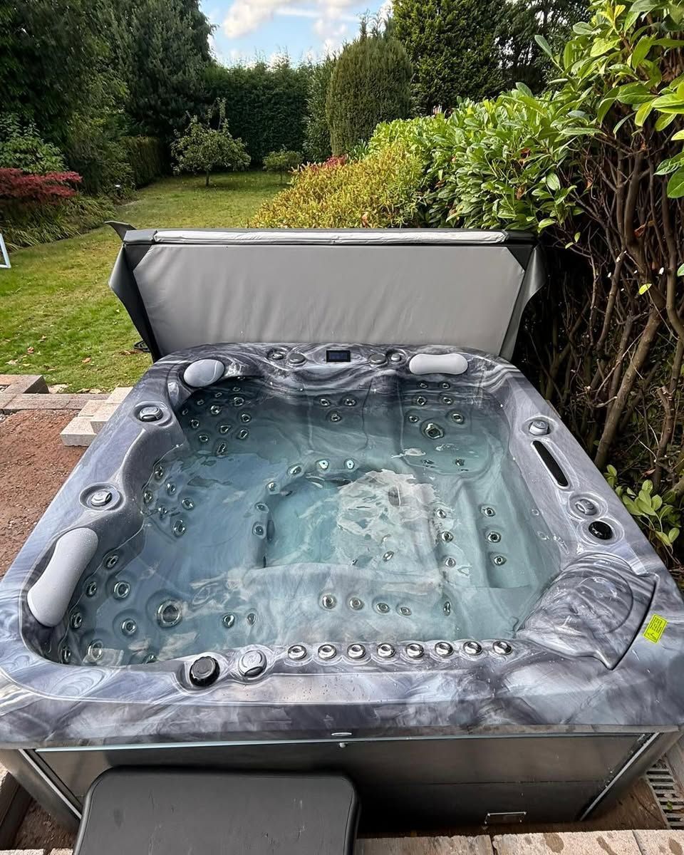 Hot tub with open gray cover, filled with water, in a backyard setting.