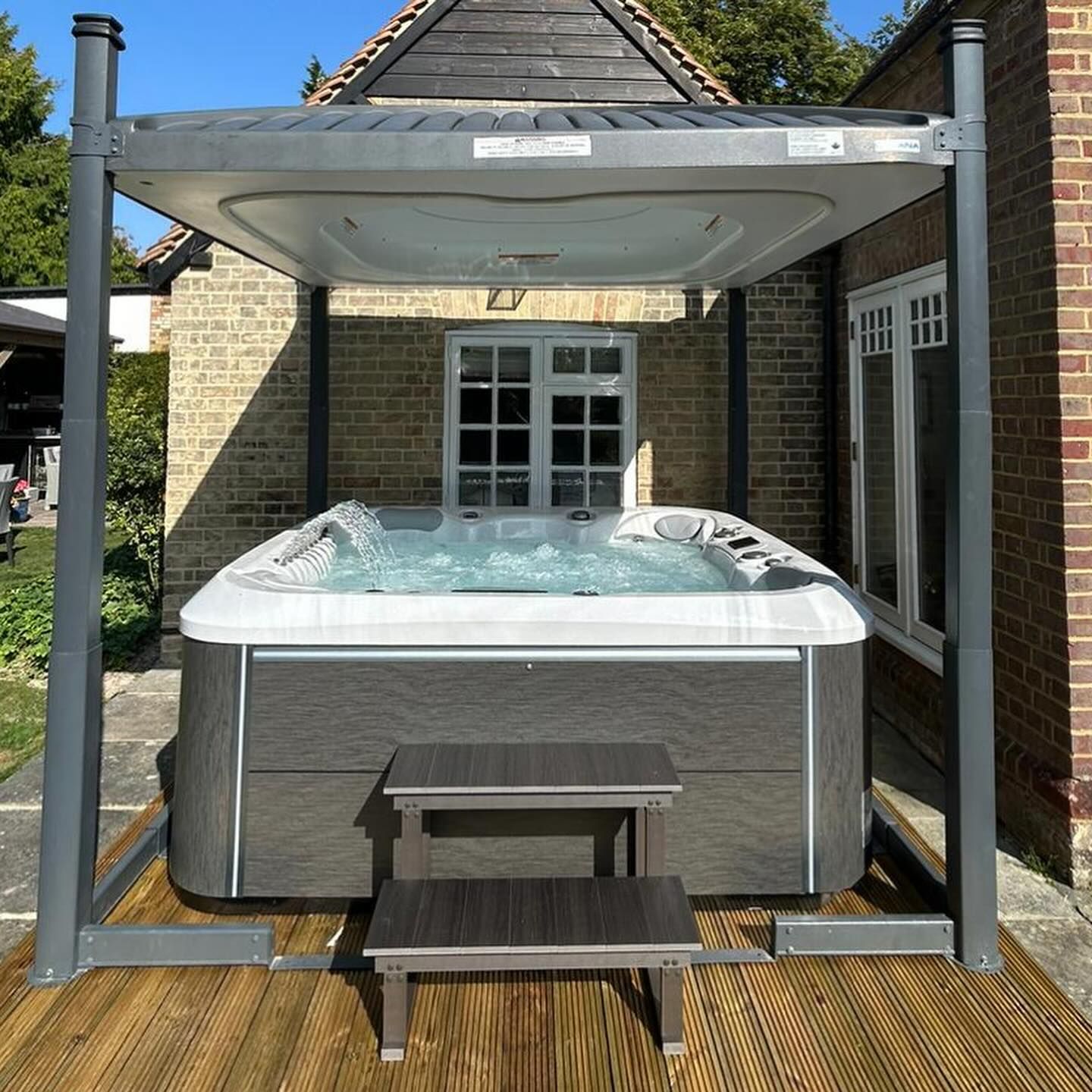 Hot tub with canopy on a wooden deck next to a brick building. Two-step stool in front.