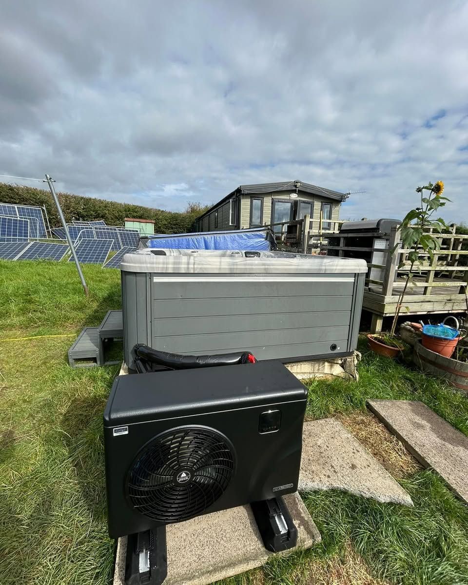 Hot tub with heat pump in grassy yard, solar panels in background, blue sky.