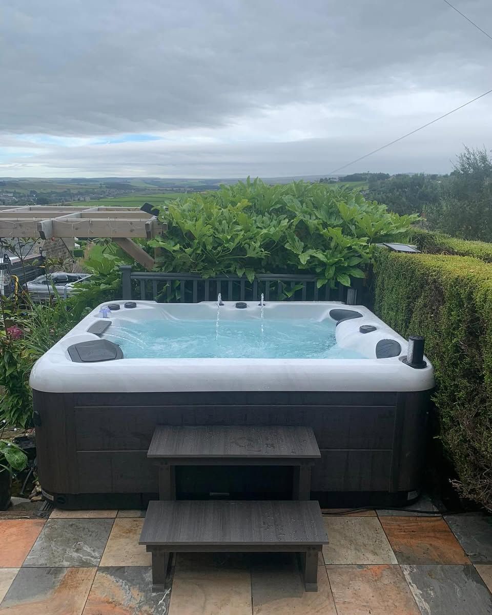 Hot tub on a patio with a view of a green landscape under a cloudy sky.