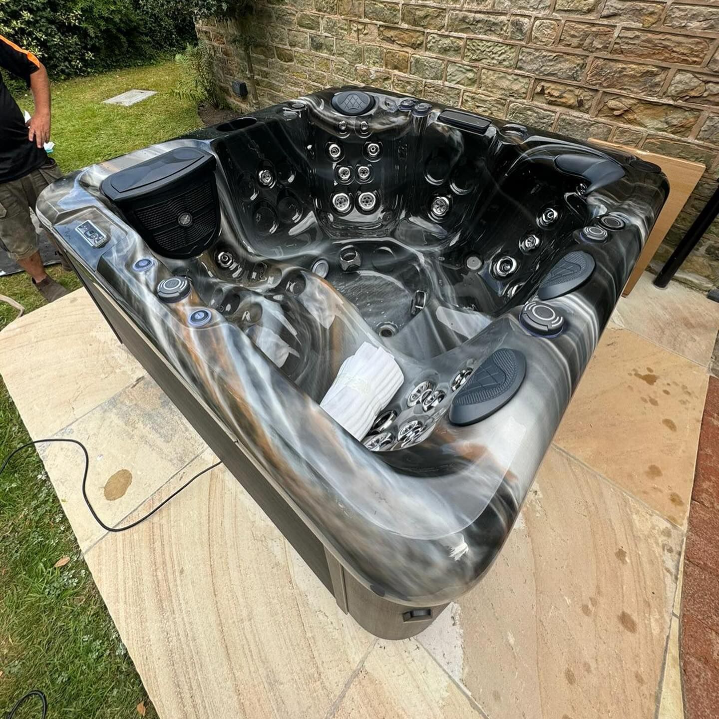 Hot tub with black and grey marbled interior, set on stone patio next to brick wall and grass.